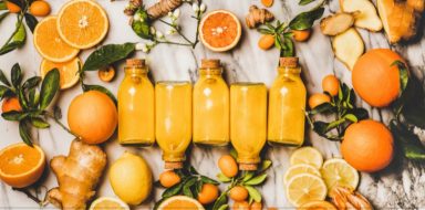 Glass bottles of orange juice laid out on a table, surrounded by slices of oranges and ginger.