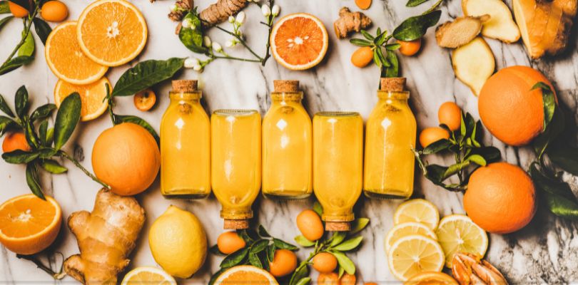 Glass bottles of orange juice laid out on a table, surrounded by slices of oranges and ginger.